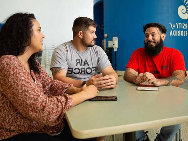 three students talking at a table in the HLS facility